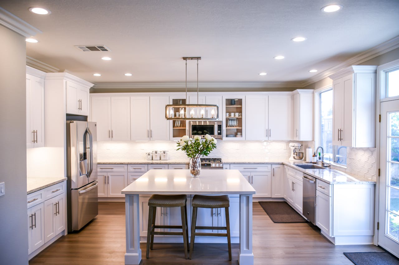 about-us-01 Spacious and elegant kitchen featuring white cabinetry, island, and stainless steel appliances.
