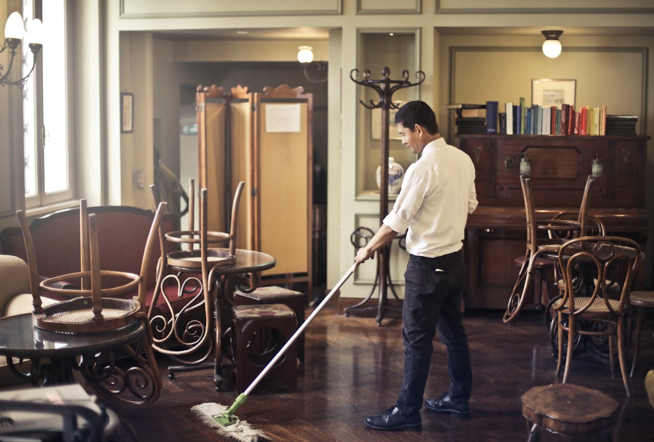 about-us-02 A man mopping the floor in a vintage style café with stacked chairs and warm lighting.